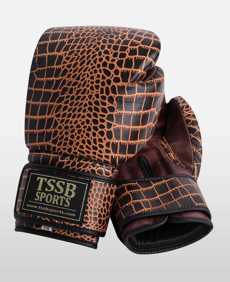 May include: A pair of brown leather boxing gloves with a crocodile pattern. The gloves have black accents and the text "TSSB SPORTS" and "www.tssbsports.com" on the wrist strap.