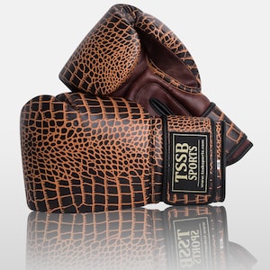 May include: A pair of brown and black boxing gloves with a crocodile pattern. The gloves have a black strap with the text "TSSB SPORTS" and the website address "www.tssbsports.com".