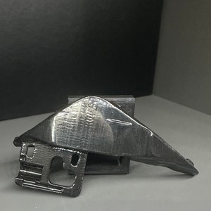 Può includere: Un oggetto nero stampato in 3D con una superficie testurizzata. L'oggetto ha una forma curva e una base piatta.