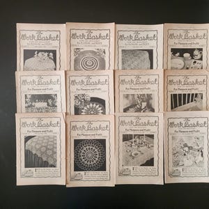 May include: A collection of vintage "Work Basket" magazines, each featuring black and white images of crochet and needlework projects. The magazines are arranged on a dark surface, showcasing their aged paper and classic design.