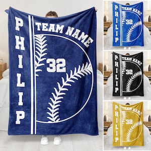 Könnte beinhalten: Eine blaue Fleece-Decke mit einem weißen Baseball-Design. Die Decke trägt den Text "TEAM NAME" und "PHILIP" mit der Nummer "32" auf dem Baseball.