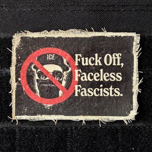May include: A rectangular patch with a distressed look, featuring the text "Fuck Off, Faceless Fascists." The patch has a red circle with a line through a figure wearing sunglasses and a hat. The word "ICE" is above the figure.