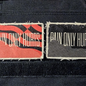 May include: Two rectangular patches with the text "PAIN ONLY HURTS". One patch has a red background with black wavy lines, the other has a black background. Both patches have white text and a distressed, frayed edge.