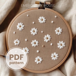 May include: A close-up of a brown embroidery hoop with white daisy flowers embroidered on a beige fabric. The text "PDF pattern" is visible in the bottom left corner of the image.