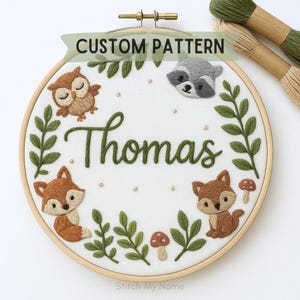 Puede incluir: Arte de aro bordado con el nombre "Thomas" en escritura verde, rodeado de criaturas del bosque, incluyendo un zorro, un búho y un mapache. El texto "CUSTOM PATTERN" está en la parte superior. El diseño está sobre un fondo blanco.