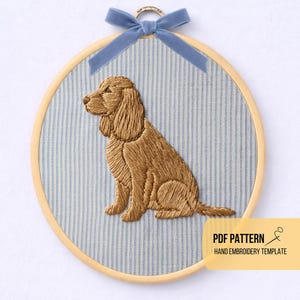 Puede incluir: Un retrato de perro bordado a mano en un aro de madera. El perro es de color marrón dorado, cosido sobre una tela a rayas azules y blancas. Una cinta de terciopelo azul está atada en la parte superior. El texto "PDF PATTERN HAND EMBROIDERY TEMPLATE" está en la esquina inferior derecha.