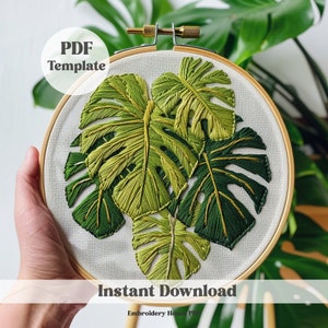 Pode incluir: Um modelo PDF para um design de bordado em aro com um grupo de folhas verdes de monstera com detalhes dourados. O texto "PDF Template" e "Instant Download" é visível na imagem.