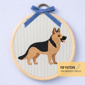 May include: Embroidered German Shepherd dog in a wooden hoop. The dog is depicted in black and tan thread, with its tongue sticking out. The background is a light blue and white striped fabric. A blue velvet ribbon is tied at the top. Text reads "PDF PATTERN HAND EMBROIDERY TEMPLATE."
