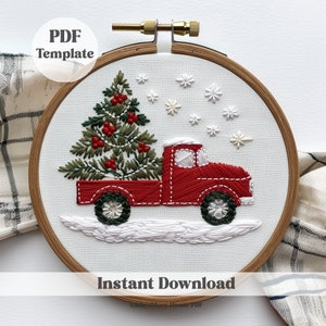 May include: Embroidered hoop art featuring a red truck carrying a green Christmas tree with red berries. The truck is driving through a snowy scene with white snowflakes.