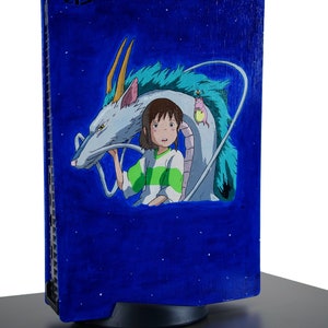 Puede incluir: Una consola de videojuegos pintada de azul con un dragón blanco y una niña con cabello castaño que lleva una camisa verde. El fondo es azul oscuro con estrellas blancas.