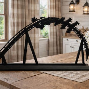 Op de afbeelding: Zwart metalen model van een achtbaan, met een gedetailleerd baanontwerp en meerdere wagons. Het model wordt tentoongesteld op een houten tafel, waarbij de ingewikkelde structuur wordt getoond. Decoratief item.