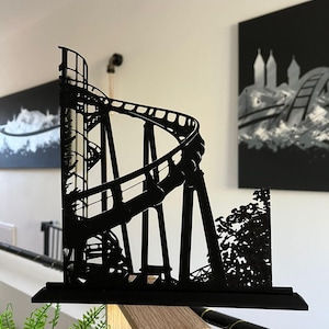 Op de afbeelding: Zwarte metalen sculptuur van een achtbaan met gedetailleerd ontwerp. De sculptuur toont een lusvormig spoor en is gemonteerd op een rechthoekige basis. Een decoratief stuk voor op een bureau of plank.