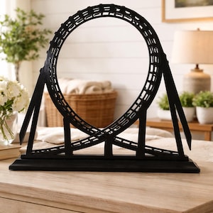 Könnte beinhalten: Schwarze Metallskulptur einer Achterbahn. Die Skulptur hat ein Looping-Design und ist auf einem rechteckigen Sockel montiert. Ein dekorativer Artikel für die Inneneinrichtung.
