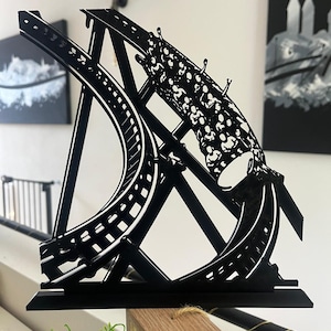 May include: A black and white decorative roller coaster sculpture. The sculpture features a detailed track design with a looping element. The piece is mounted on a black base and is set against a neutral background.