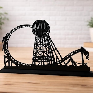 May include: Black laser-cut wooden sculpture of a roller coaster with a spherical tower. The sculpture is on a rectangular base and features a loop-de-loop and a drop. The design is a silhouette.