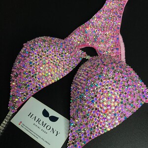 May include: Pink bikini top with crystal embellishments. The top is made of a stretchy fabric and has a halter style strap. The top is covered in iridescent crystals that sparkle in the light. The top is a competition style bikini top.