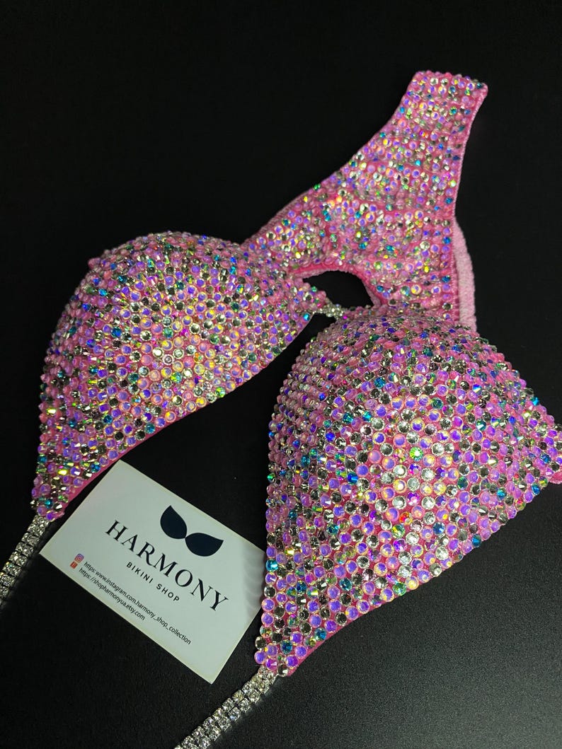 May include: Pink bikini top with crystal embellishments. The top is made of a stretchy fabric and has a halter style strap. The top is covered in iridescent crystals that sparkle in the light. The top is a competition style bikini top.