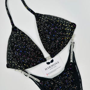 May include: Black bikini with iridescent rhinestones and a black fabric strap with silver rhinestones. The bikini is on a white background. The text "HARMONY BIKINI SHOP" is on a white card in the lower right corner of the image.