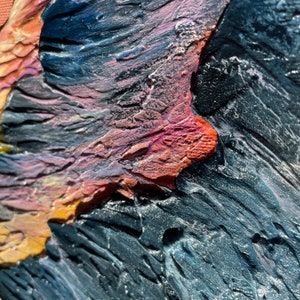 May include: Close-up of a textured abstract painting with visible brushstrokes. The artwork features a palette of colors including orange, pink, blue, and black. The thick application of paint creates a three-dimensional effect.