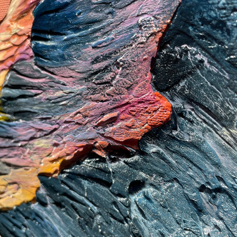 May include: Close-up of a textured abstract painting with visible brushstrokes. The artwork features a palette of colors including orange, pink, blue, and black. The thick application of paint creates a three-dimensional effect.