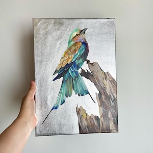 Puede incluir: Una pintura de un pájaro colorido posado en una rama. El pájaro tiene plumas azules, verdes y marrones. El fondo es de color plateado metálico.
