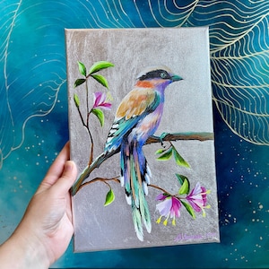 Puede incluir: Una pintura colorida de un pájaro con una cola larga posado en una rama con flores rosas. El pájaro tiene plumas azules, verdes, moradas y naranjas. El fondo es de color plateado metálico.