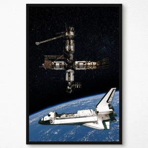 May include: A framed print featuring a space shuttle and a space station against a backdrop of stars and the Earth's curvature. The space shuttle is white with black accents, and the space station is a complex structure with multiple modules.