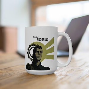 Könnte beinhalten: Weiße Keramik-Tasse mit einer Illustration eines Mannes und dem Text "MAN of PROGRESS". Das Design ist in Schwarz und Olivgrün gehalten, mit einem Zahnrad und einem Sonnenstrahlen-Motiv.