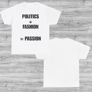 Può includere: T-shirt bianche con la scritta "POLITICS + FASHION = PASSION" in nero. L'immagine mostra il davanti e il retro della maglietta. Le magliette sono esposte su una superficie a venatura di legno chiaro.