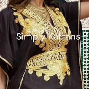 May include: A black kaftan with gold embroidery. The embroidery features intricate floral designs and a V-neckline. The text "Simply Kaftans" is visible on the garment.