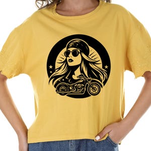 May include: A yellow t-shirt with a black and white graphic of a woman wearing sunglasses and a cap riding a motorcycle. The graphic is inside a circle with stars.