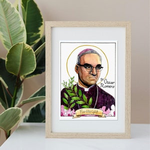 Puede incluir: Una pintura al agua enmarcada de San Oscar Romero, un arzobispo católico. La pintura lo representa con una sotana morada y una mitra, con un halo detrás de él. El texto "St. Oscar Romero" está escrito debajo de él.