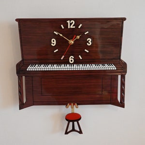 May include: A wooden wall clock shaped like a brown upright piano with a white and black keyboard. The clock face has Roman numerals and a red second hand.