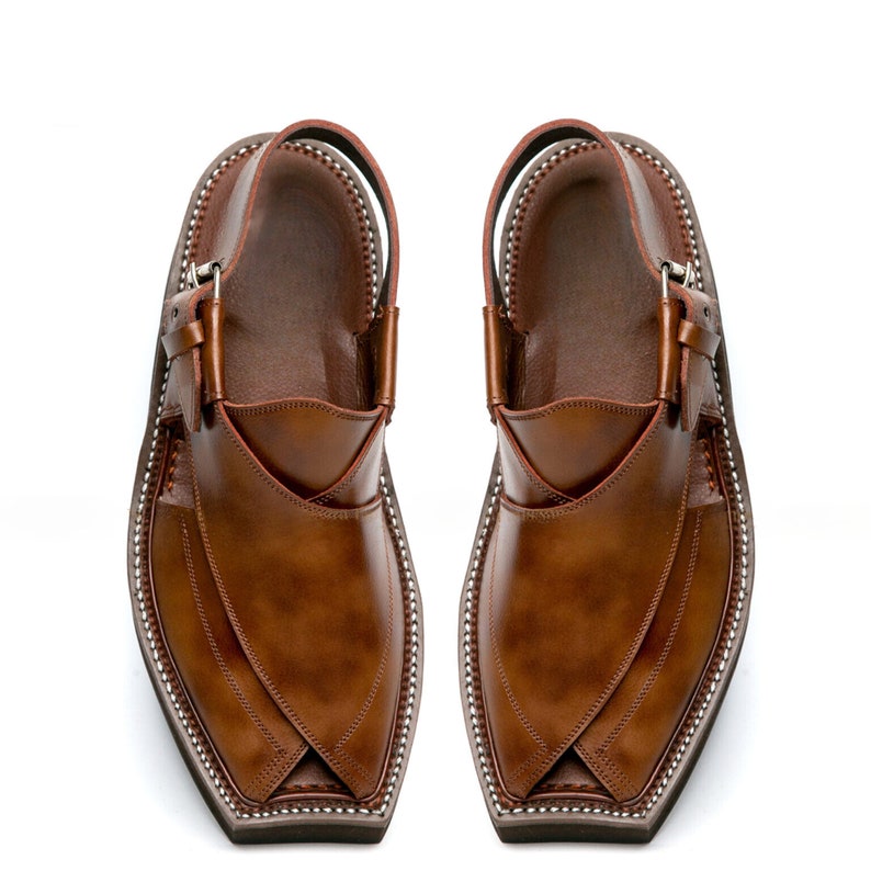 May include: A pair of brown leather shoes with pointed toes and a strap across the ankle. The shoes have a decorative stitching pattern around the edges.