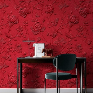 Può includere: Carta da parati rossa in rilievo floreale con un motivo ripetuto di rose e foglie. Il design strutturato crea un effetto 3D. Una scrivania nera con una lampada, una sedia e oggetti decorativi sono di fronte alla carta da parati.