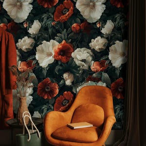 May include: An orange armchair with wooden legs is positioned in front of floral wallpaper with large white and red poppies. A green tote bag with rope handles and a small side table with a vase are also visible.