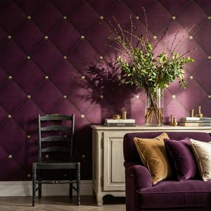 May include: A luxurious living room scene featuring a deep purple tufted wall with gold button accents. A black wooden chair, a white cabinet, and a purple corduroy sofa with decorative pillows complete the elegant decor. A vase of greenery adds a natural touch.