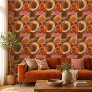 May include: A living room scene featuring a burnt orange sofa, a wooden coffee table, and a patterned wallpaper. The wallpaper has a repeating design of abstract brushstrokes in shades of orange, pink, and white. A woven rug and a potted plant complete the decor.
