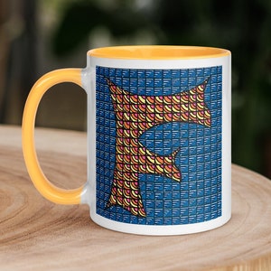 May include: A white ceramic mug with a yellow rim and handle. The mug features a colorful geometric design of the letter "F" on a blue background.