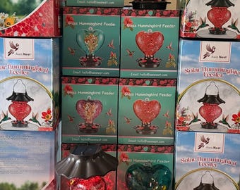 Könnte beinhalten: Eine Sammlung von verpackten Solar-Kolibri-Futterstellen mit herzförmigen Glasbehältern in Rot und Türkis. Die Verpackung zeigt den Produktnamen Solar Hummingbird Feeder und die Marke Fresh Nest mit Abbildungen der Futterstellen.
