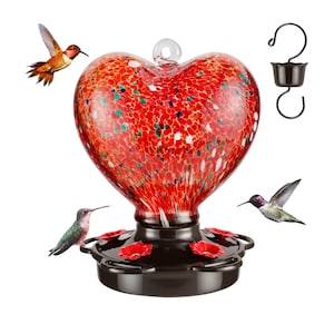 May include: Red heart-shaped glass hummingbird feeder with a brown metal base and four feeding ports. Three hummingbirds are flying around the feeder.
