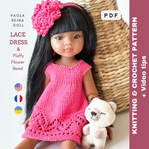 Pode incluir: Uma boneca Paola Reina vestindo um vestido de renda rosa tricotado e uma faixa de cabelo de flores combinando. A boneca tem cabelo preto e segura um pequeno ursinho de pelúcia branco. A imagem inclui o texto "Vestido de renda & Faixa de flores fofa".