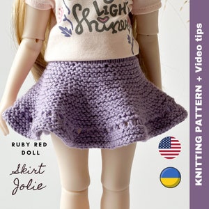 May include: A lilac-coloured, knitted skirt with a flared design. The skirt is part of a doll's outfit, paired with a light pink t-shirt. The text "Skirt Jolie" is visible on the image. The image also includes the text "Knitting Pattern + Video tips".