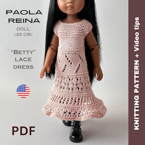 Könnte beinhalten: Eine Puppe in einem rosa Spitzenkleid. Die Puppe ist 33 cm groß und hat lange schwarze Haare. Das Kleid hat ein detailliertes Lochmuster. Auf dem Bild steht "PAOLA REINA DOLL (33 CM)", "BETTY LACE DRESS" und "PDF".