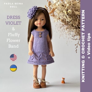 May include: A purple knitted dress with a crocheted flower headband for a Paola Reina doll. The dress has a lace pattern on the bottom and the headband is a fluffy flower. The doll is wearing brown shoes.