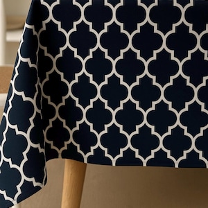 Könnte beinhalten: Marineblaue Tischdecke mit weißem Vierpassmuster. Die Tischdecke ist über einem Holztisch drapiert und zeigt das geometrische Design. Der Stoff scheint mittelschwer zu sein und ist für den täglichen Gebrauch geeignet.
