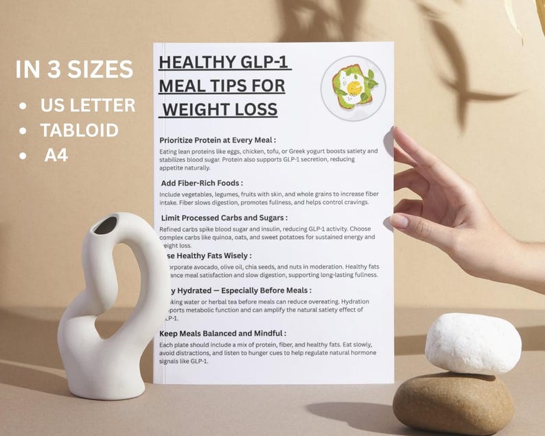 May include: A white paper with the title "HEALTHY GLP-1 MEAL TIPS FOR WEIGHT LOSS" and meal tips. A white ceramic vase and two stacked stones are in the foreground. The paper is held by a hand.