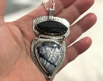 Puede incluir: Collar colgante de plata hecho a mano con dos piedras. La piedra superior es negra y oblonga, y la inferior tiene forma de lágrima con un patrón blanco y negro. El colgante cuelga de una delicada cadena de plata.