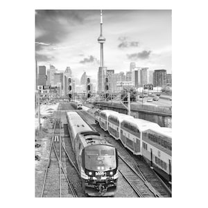 May include: Black and white photograph of a cityscape featuring a train track with two trains in the foreground. The CN Tower is visible in the background, along with other skyscrapers. The sky is overcast.
