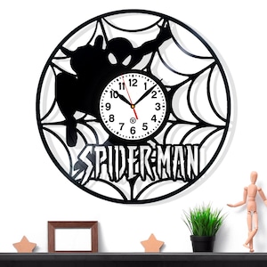 Pode incluir: Relógio de parede preto do Homem-Aranha com um design de teia de aranha. O mostrador do relógio é branco com números e ponteiros pretos. A palavra "SPIDER-MAN" é exibida abaixo.